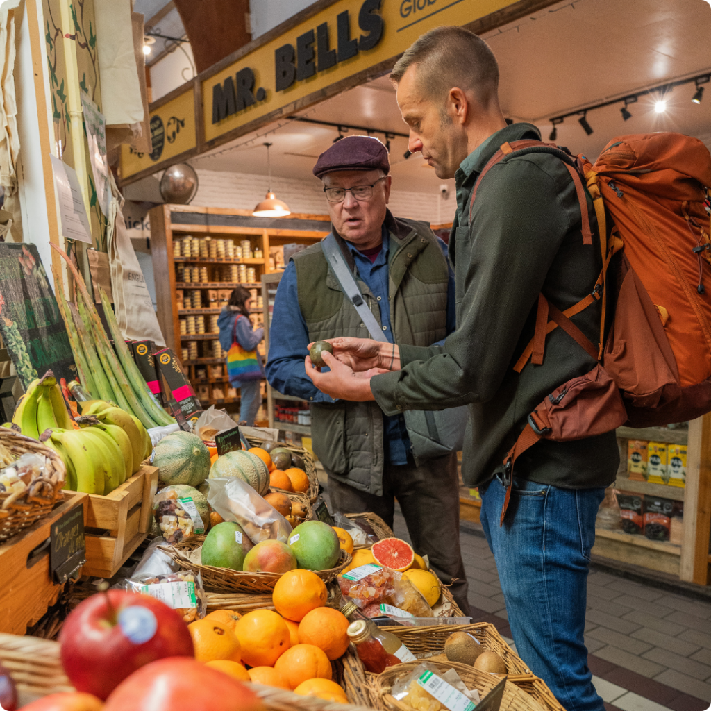 a photo of two men shopping at a local market for food to cook in cork ireland during an outdoor eats tv shoot