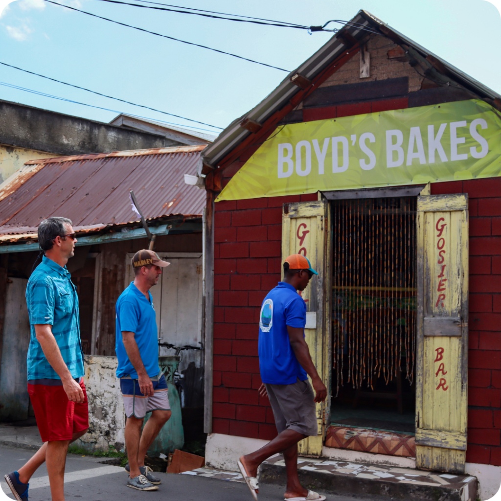 three men walking into a local business in dominica called boyds bakes while filming for a tv show facing waves with ken whiting